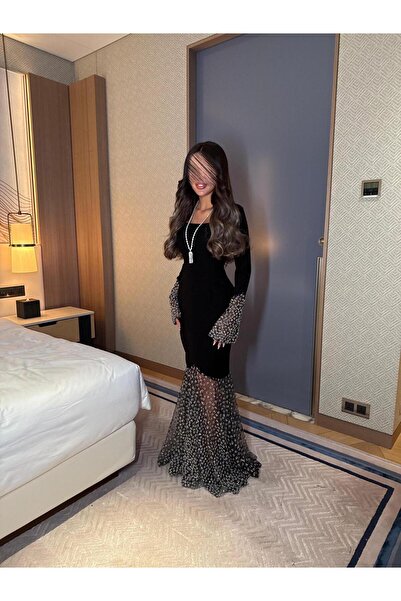 Riva A long black evening dress with embellished sleeves and a sheer, studded train.