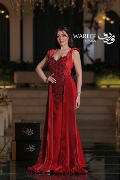WAREEF FASHION A long royal red crepe evening gown embroidered with pearls, featuring a side pleated train and an elegant back tie.