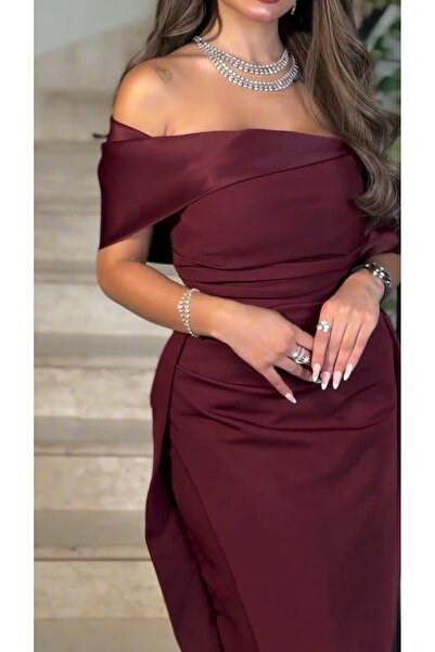 Riva The dress has an open neckline, an elegant burgundy color, a side slit, and attractive pleats.