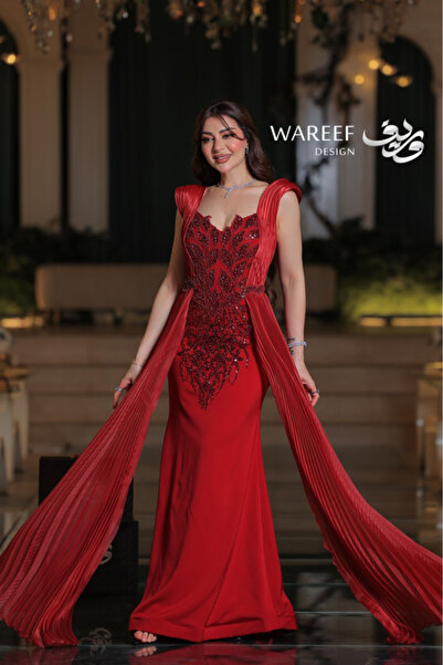 WAREEF FASHION A long royal red crepe evening gown embroidered with pearls, featuring a side pleated train and an elegant back tie.