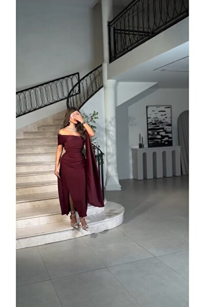 Riva The dress has an open neckline, an elegant burgundy color, a side slit, and attractive pleats.