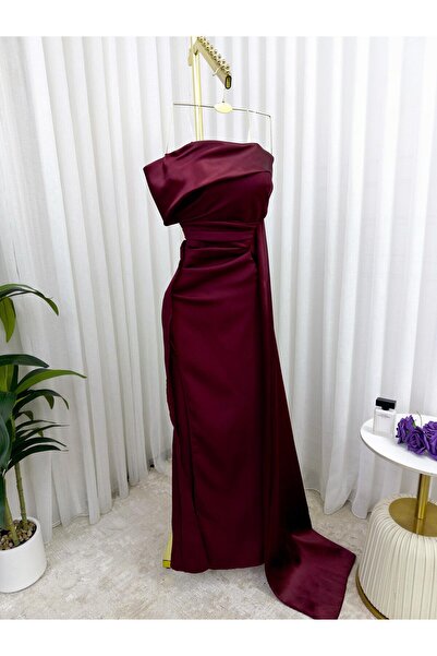 Riva The dress has an open neckline, an elegant burgundy color, a side slit, and attractive pleats.