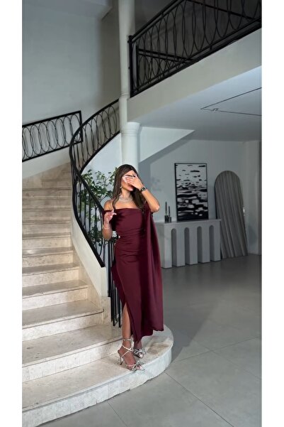 Riva The dress has an open neckline, an elegant burgundy color, a side slit, and attractive pleats.