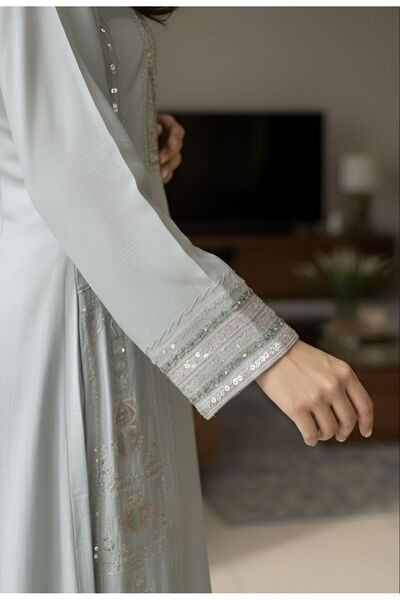 ISHRAQAT AL-AMAL A long, light blue jalabiya with rich embroidery on the chest and sleeves, creating a beautiful drape, perfect for gatherings and special occasions.