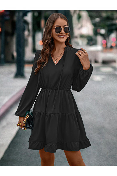 GENERAL A short, casual black swing dress with a V-neck and long sleeves, sui...