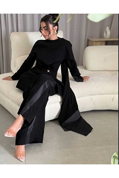 REVE جمبسوت أسود دراماتيكي بقطعة كيب منسدلة، خصر محدد، وأرجل واسعة.