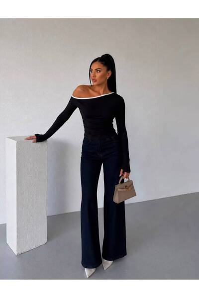 model tek omuzu açık, asimetrik kesimli ve uzun kollu siyah Boyun kısmındaki beyaz şerit detayı siyahla kontrast oluştururken parça vücudu sarıyor.