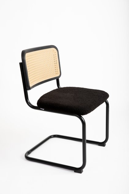 A fixed chair with a strong plastic rattan back and a black bouclé seat