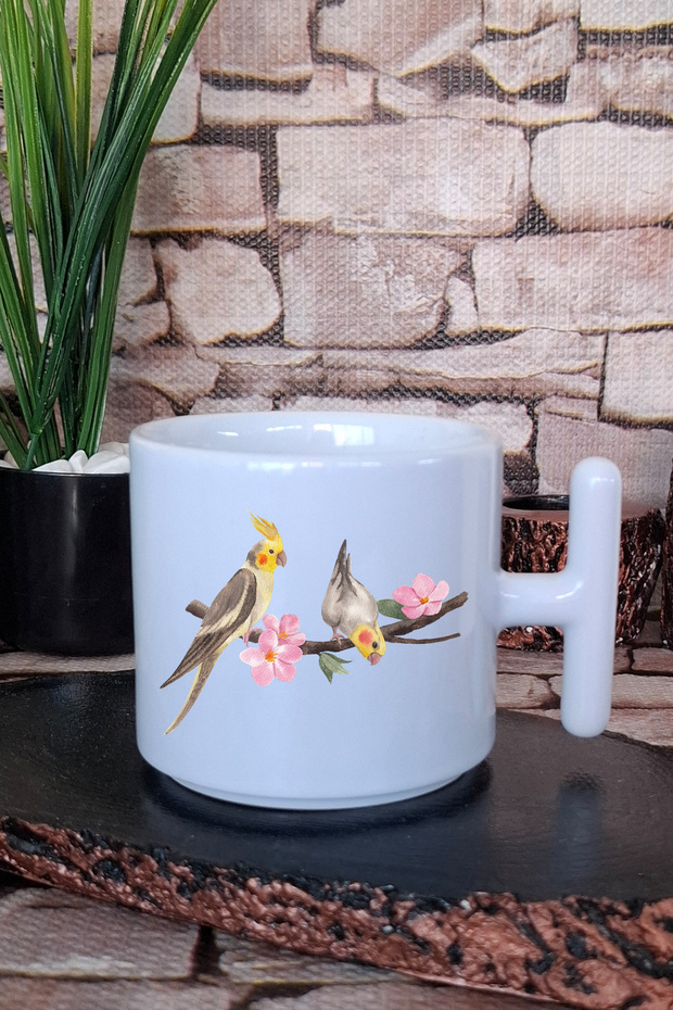 كوب لاتيه مطبوع عليه طائر يزقق على الأغصان مع مقبض على شكل حرف T