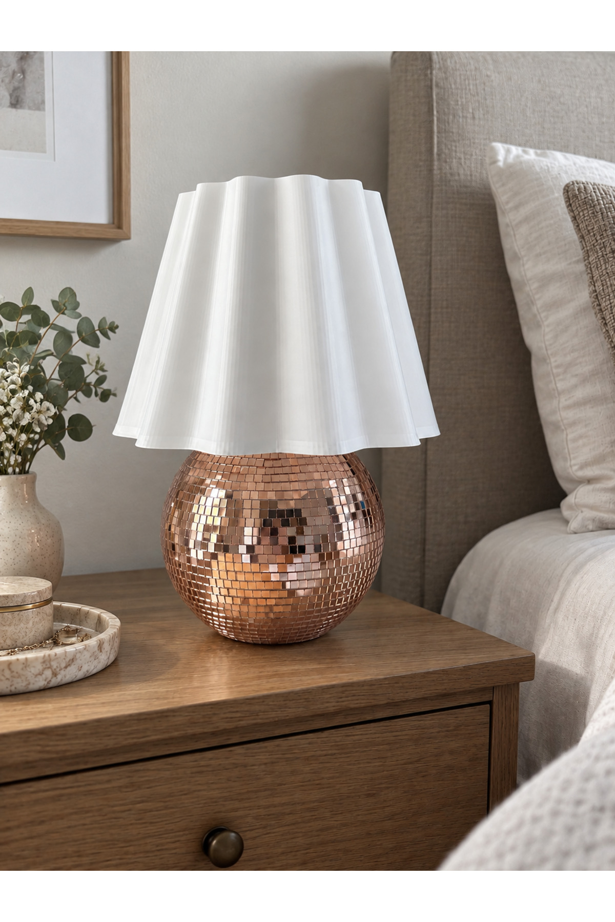 Disco Wave Abajur, bakır mozaik küre taban ve beyaz pileli başlıkla komodin üzerinde.